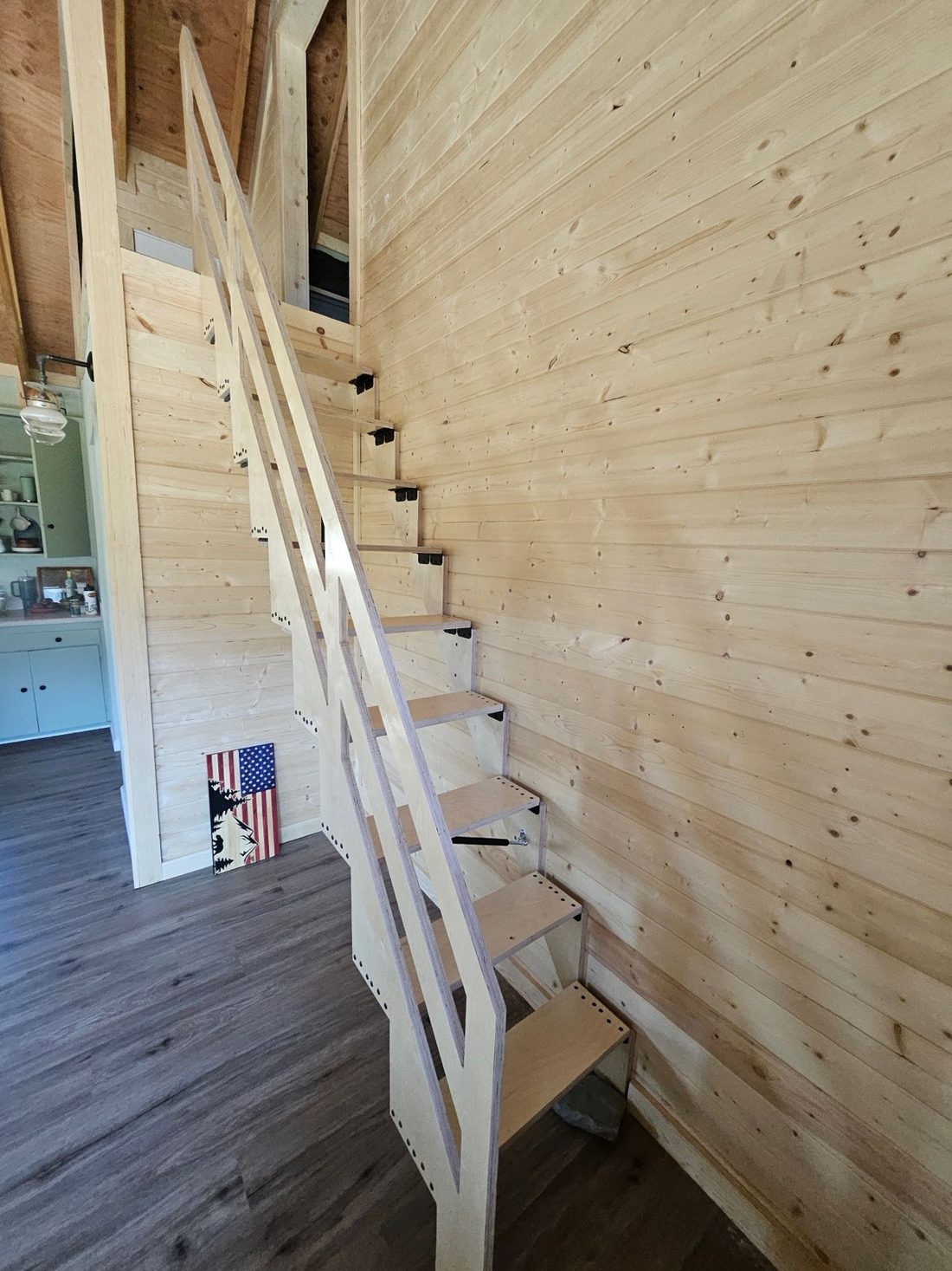 A folding stair folded down in a pine-paneled cabin, ready to climb to the loft